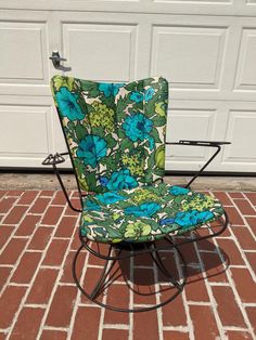 a blue and green chair sitting on top of a red brick floor next to a garage door