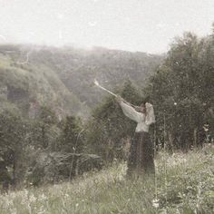 a woman standing on top of a lush green hillside next to trees and bushes in the rain