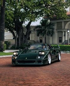 a green sports car is parked in front of a large building with trees and bushes