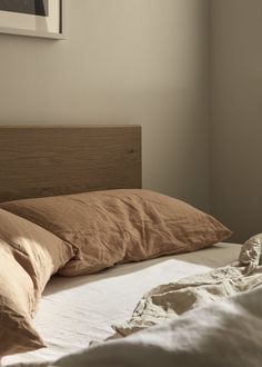 an unmade bed with brown sheets and pillows on it in a room that has white walls