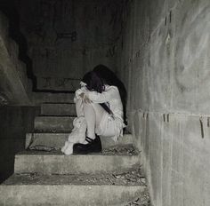 a person sitting on some stairs with their head in her hands and the other hand holding something