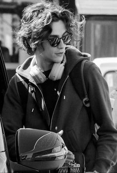 black and white photograph of a woman with headphones in her ears, leaning against a car door