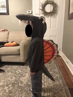 a young boy wearing a shark costume standing in front of a living room with his mouth open