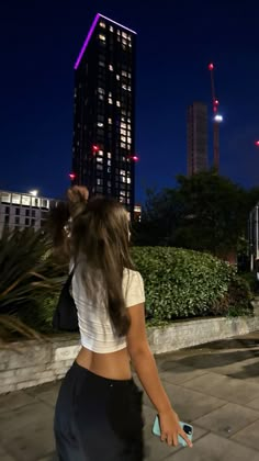 a woman is walking down the sidewalk in front of a building at night with her back to the camera