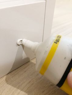 a hand is holding a white and yellow lightbulb near a wall outlet on a wood floor