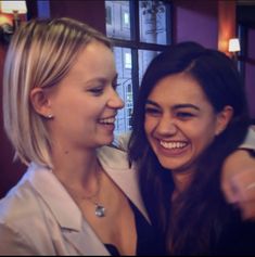 two women smiling and pointing at something in front of them with their arms around each other