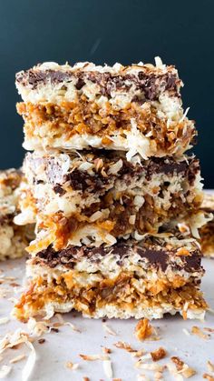 three pieces of chocolate and coconut bars stacked on top of each other with nuts scattered around them