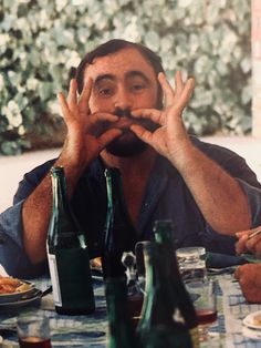 a man sitting at a table with two beer bottles in front of him and his hands up to his mouth