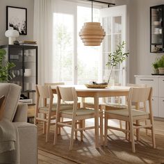 a dining room table and chairs in front of a large window with potted plants on it