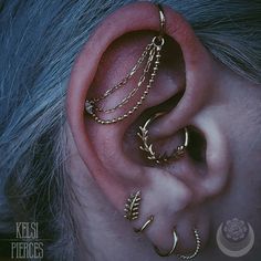 an ear with three gold chains attached to the middle one and two different piercings on each side