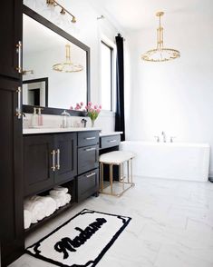 a bathroom with black cabinets and white marble flooring is pictured in this image, there are two chandeliers hanging above the bathtub