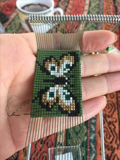 a hand is holding a small beaded object in the shape of a dog on a green background