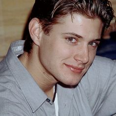 a close up of a person wearing a gray shirt and looking at the camera with a smile on his face