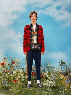 a man standing on top of a lush green field next to wildflowers wearing a gucci jacket