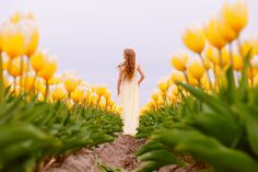 a woman standing in the middle of yellow tulips with her back to the camera