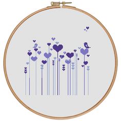 a cross stitch pattern with purple hearts and flowers on white fabric in a wooden hoop