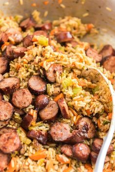 a bowl filled with rice and sausage next to a spoon