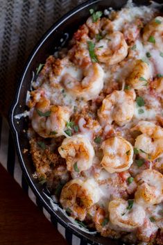 a skillet filled with shrimp and cheese on top of a striped cloth next to a wooden table