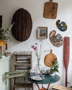 an old table with some flowers on it in front of pictures and other things hanging on the wall