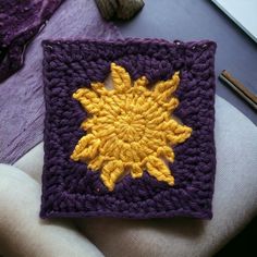 a crocheted square with a yellow and purple flower on it next to knitting needles