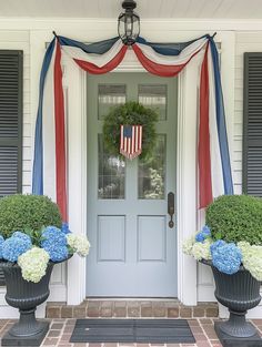 two large urns filled with flowers sit in front of a door decorated for the fourth of july