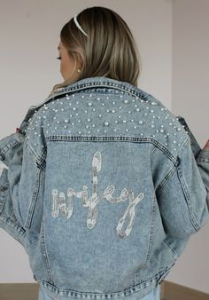 the back of a woman wearing a jean jacket with studded letters and words on it