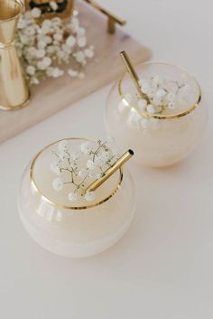 two white vases with flowers in them sitting on a table next to a tray