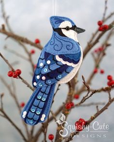 a blue and white bird ornament hanging from a tree branch with red berries