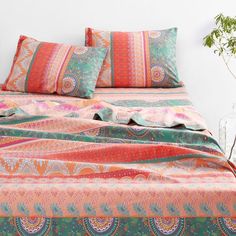 a bed with colorful sheets and pillows on it's headboard, next to a potted plant