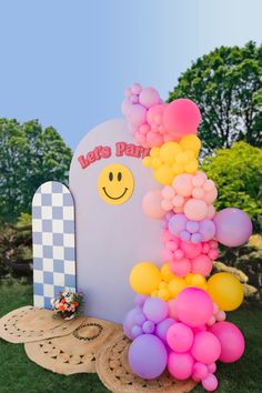 a bunch of balloons that are sitting in the grass near a sign with a smiley face on it