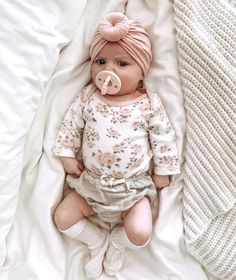 a baby wearing a pink turban laying on top of a bed next to a white blanket