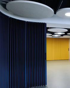 an empty room with yellow and blue curtains on the walls, and round lights hanging from the ceiling