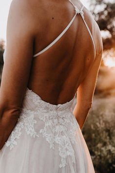 the back of a bride's dress as she stands in a field at sunset