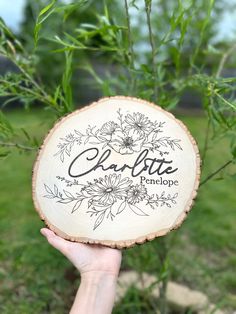 someone holding up a wooden slice with the word charlotte on it in front of some grass