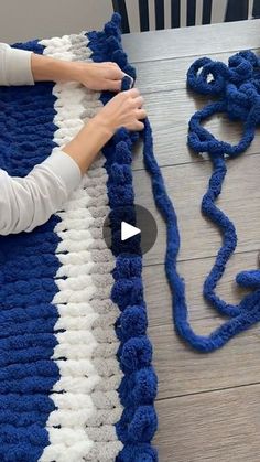 a woman is crocheting a blue and white blanket on the floor with yarn