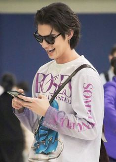 a young man wearing sunglasses looking at his cell phone while holding a purse and smiling