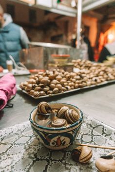 some food that is on a table with people in the back ground and one bowl full of snails