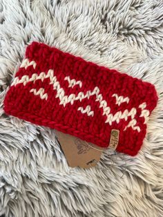 a red and white knitted headband laying on top of a fur rug next to a tag