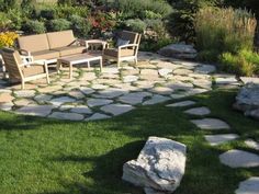 a stone patio with chairs and a couch in the middle is surrounded by green grass