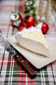 a slice of cheesecake on a plate next to a fork and christmas tree ornament