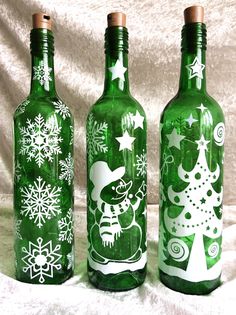 three green glass bottles decorated with snowflakes and christmas tree designs are on a white background