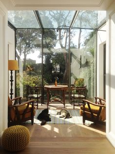 the sun shines through an open glass room with chairs and a table in it