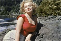 a woman sitting on top of a rock next to a river with trees in the background