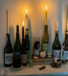 candles and wine bottles on a table in front of a white wall with the candle lit