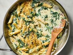 a skillet filled with pasta and spinach covered in white sauce on top of a marble counter