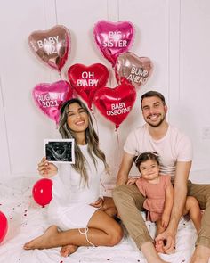 a man, woman and child are sitting on a bed with balloons in the shape of hearts