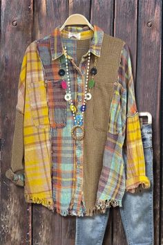 a colorful shirt and jeans hanging on a wooden wall with beads, necklaces and other accessories