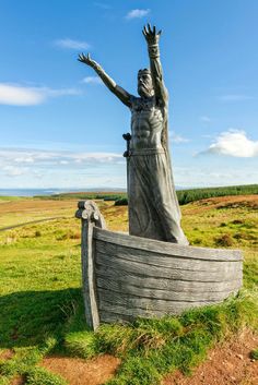 a statue of a woman standing next to a boat on top of a lush green field