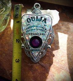 "This is a Ouija Board Mood Color Change Resin Faux White Opal Planchette Hand Made Necklace. It features a hand cast resin planchette with faux opal prismatic flakes that has a glass mood stone for the \"viewer\". It is set on a 3 inch antiqued silver tone setting. It comes with an 18 inch stainless steel chain. If you need the chain longer or shorter please let me know in the notes section of your order. This necklace is hand made by me. The \"viewer\" on the necklace is a glass mood stone tha