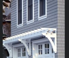 a white pergolan attached to the side of a house with windows and doors